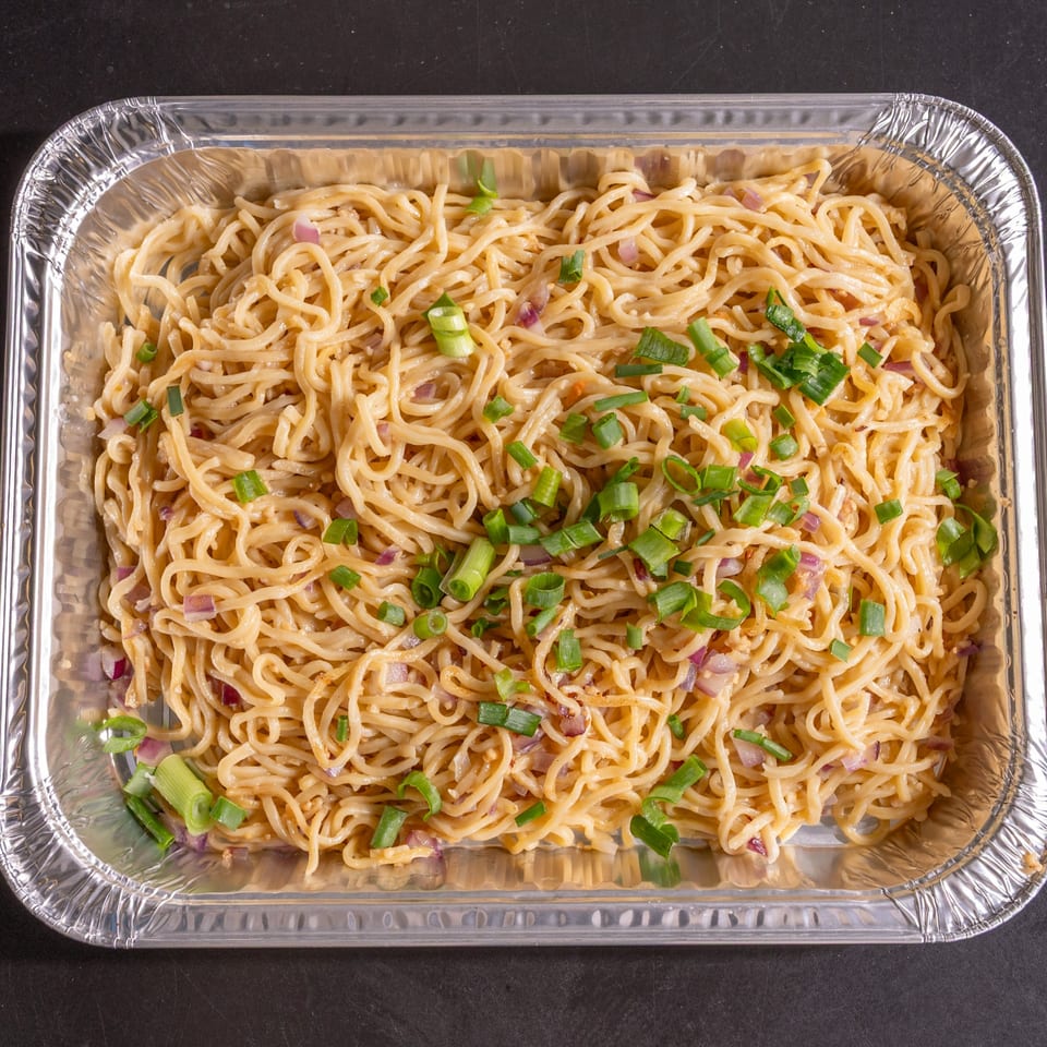 Noodles with chopped red onions and green onions in a silver foil takeout container.