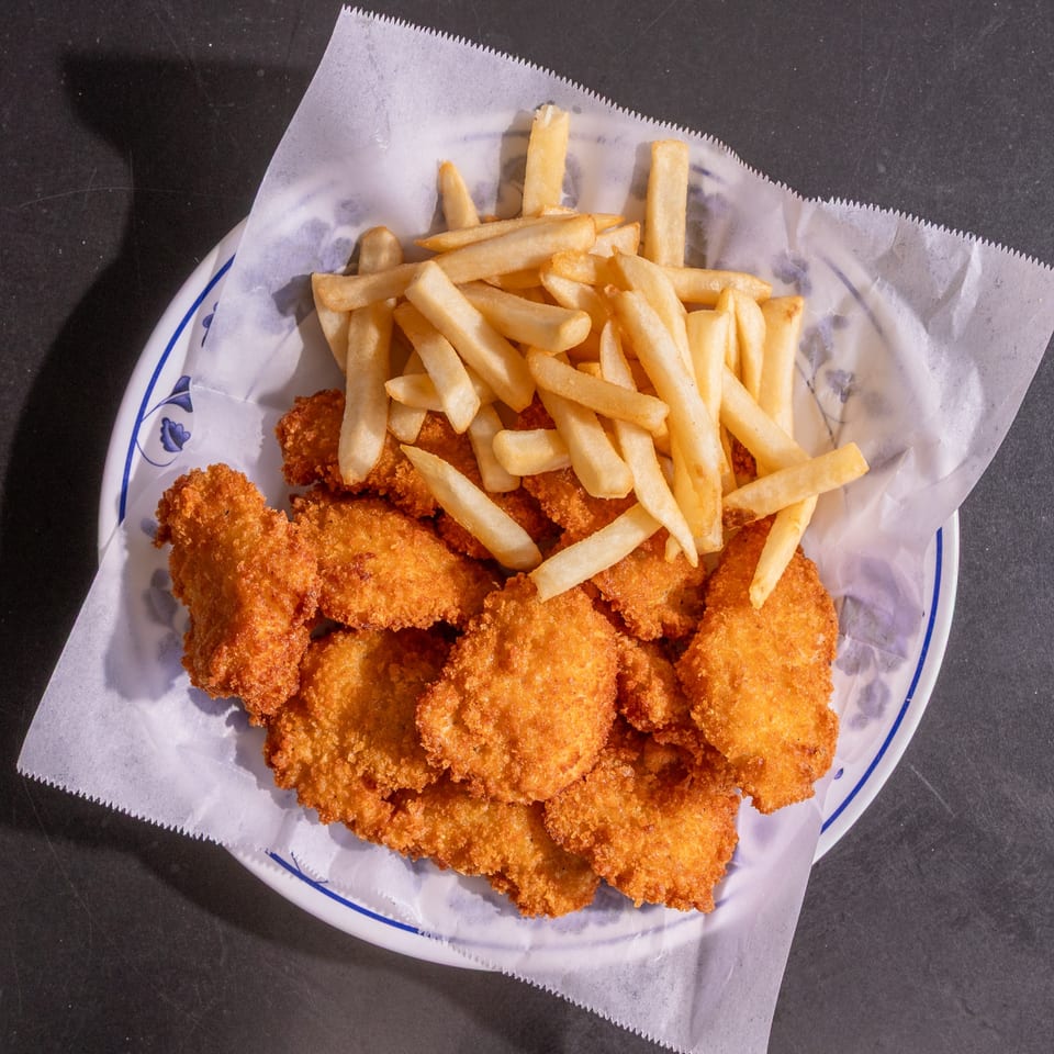 A white plate with blue trim holds a serving of golden-brown fried chicken nuggets and french fries.