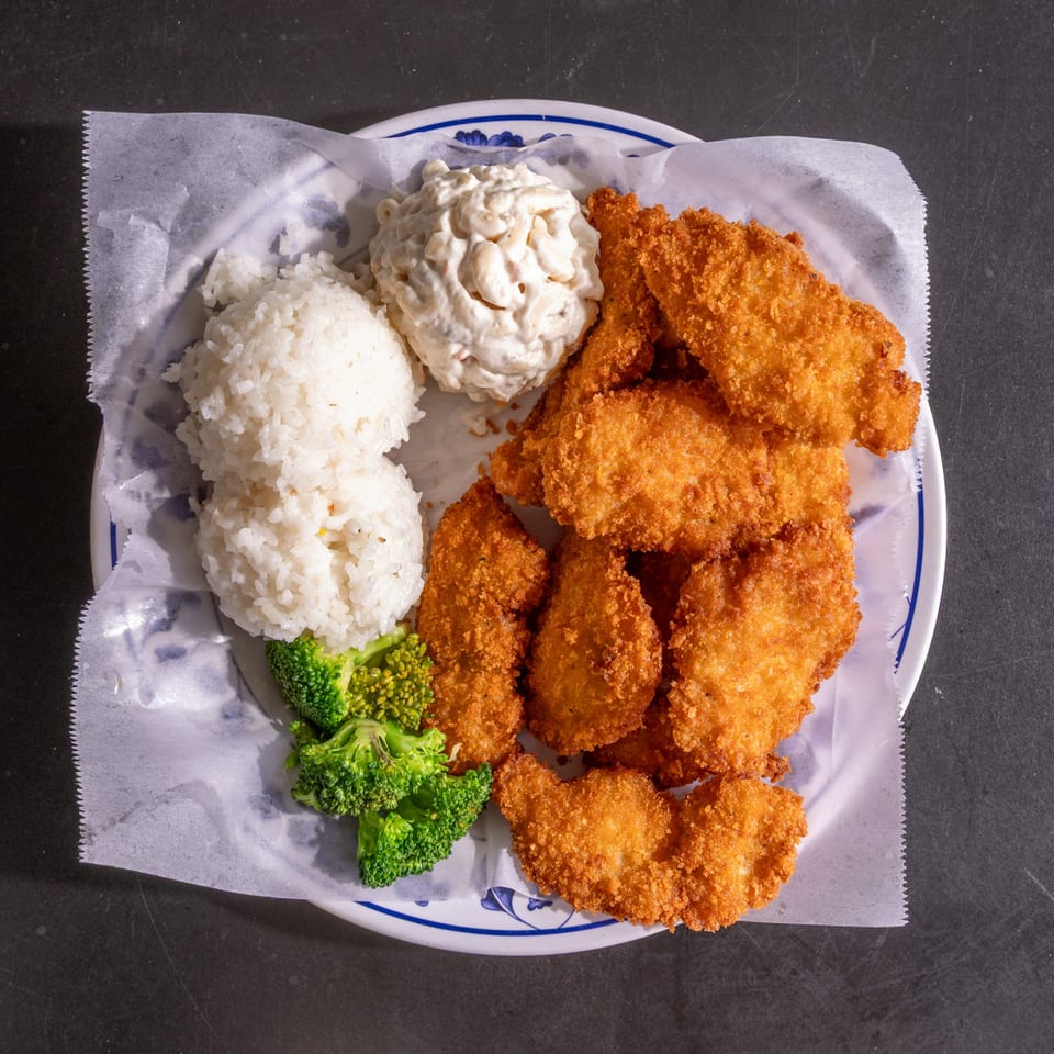 Plate of crispy fried chicken, white rice, macaroni salad, and steamed broccoli on dark background.