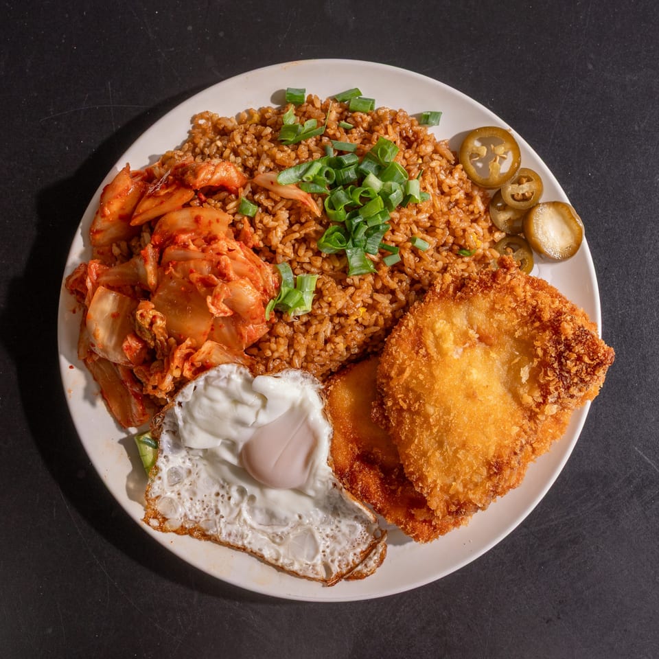 Kimchi fried rice with fried chicken, a sunny-side-up egg, and pickled jalapeños on a white plate.