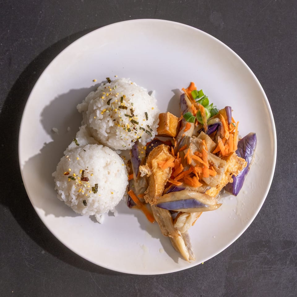 Two scoops of white rice with furikake next to stir-fried eggplant, tofu, and shredded carrots.