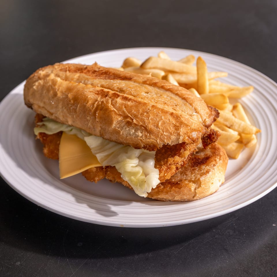 Crispy fried chicken sandwich with cheese and lettuce on a baguette, served with french fries.